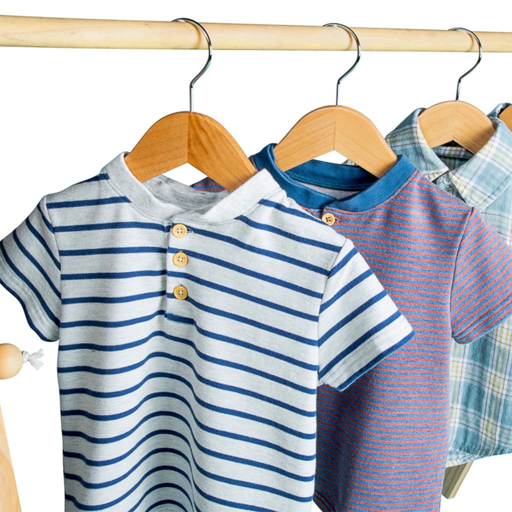 white shirt with blue stripes and 3 tan buttons on a wooden hanger with blue and red striped shirt behind it.
